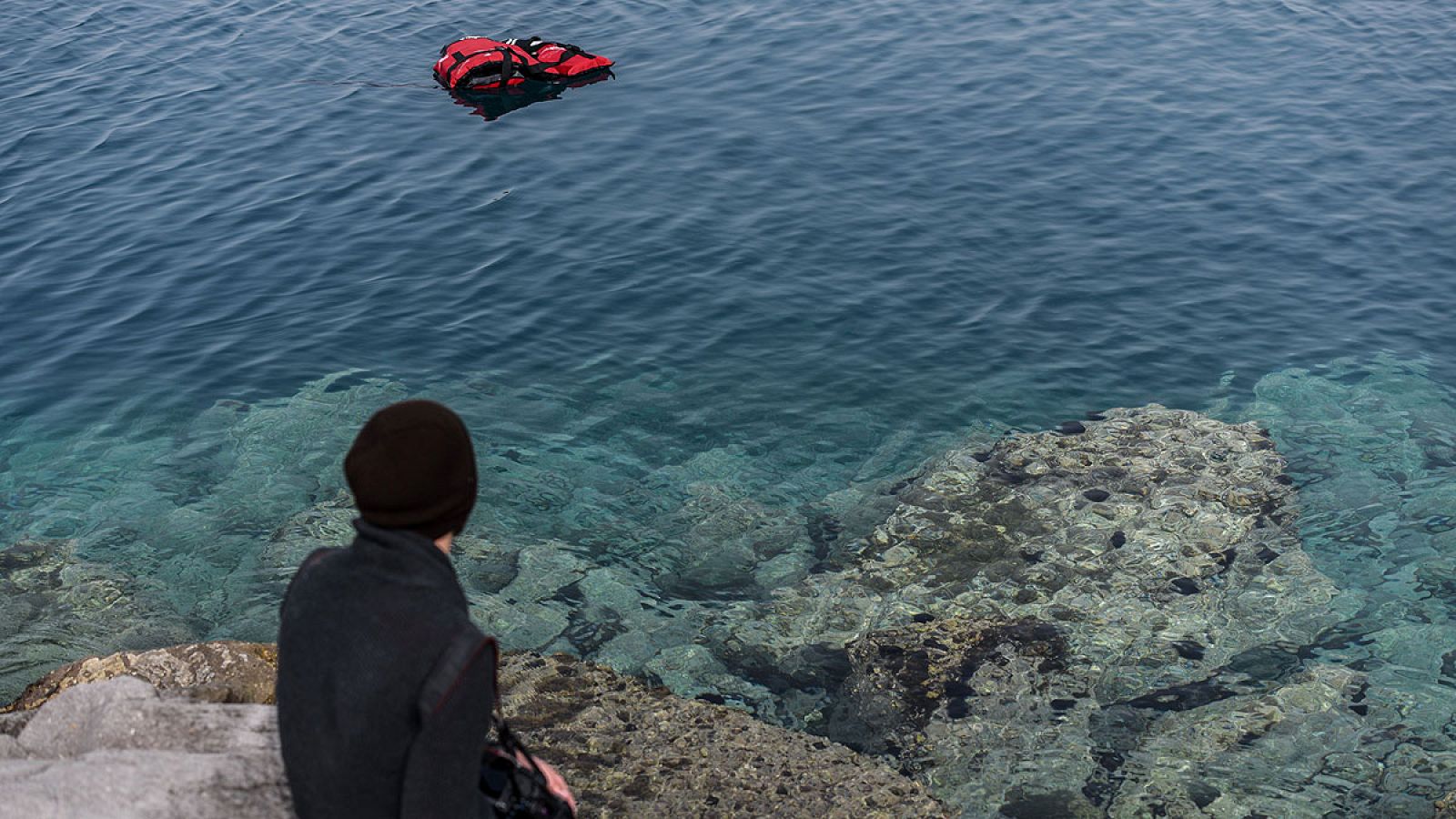 Un hombre observa un chaleco salvavidas en el mar Egeo desde el puerto turco de Dikili