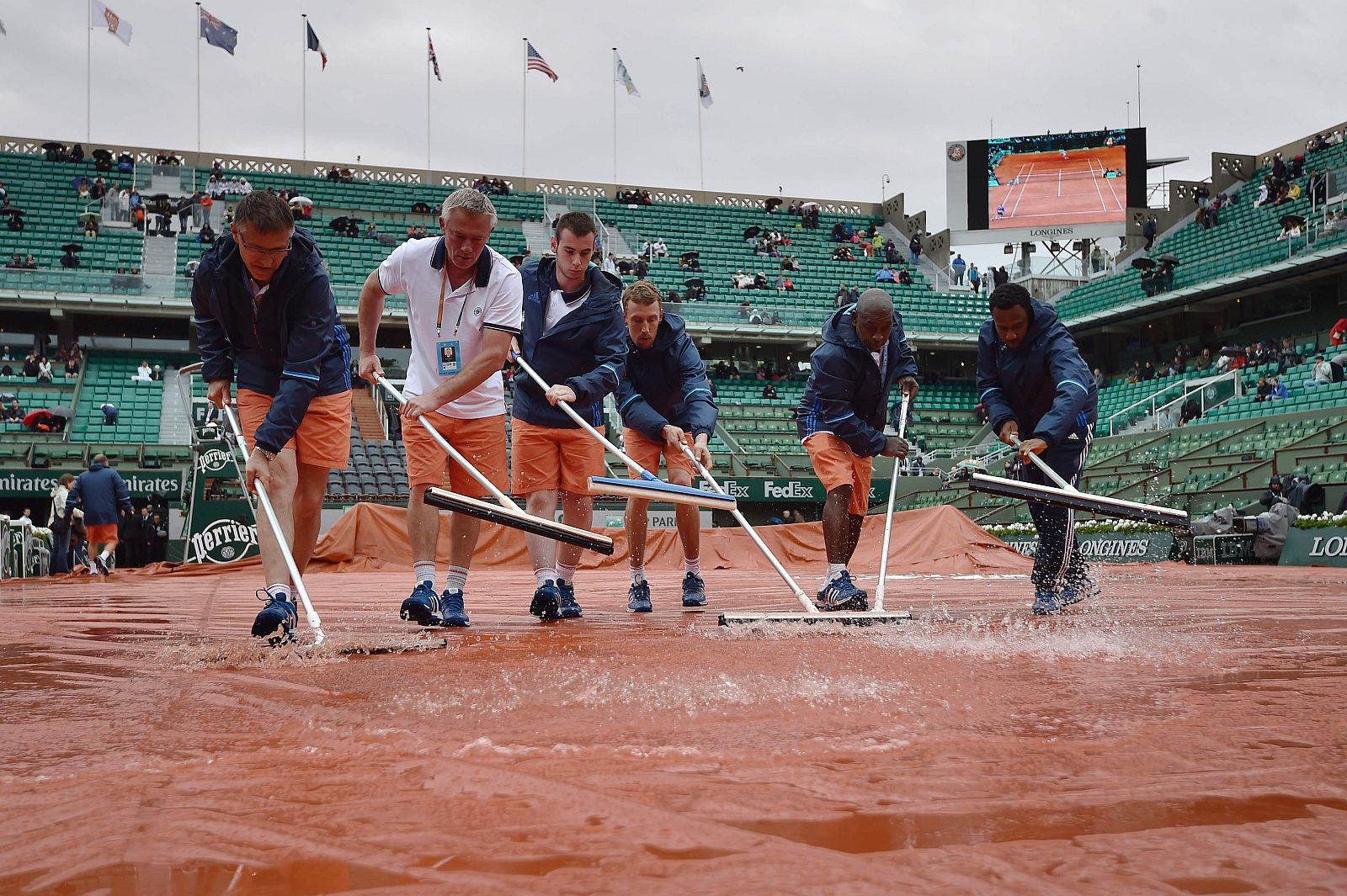 Un grupo de pisteros achica agua en la pista central de Roland Garros