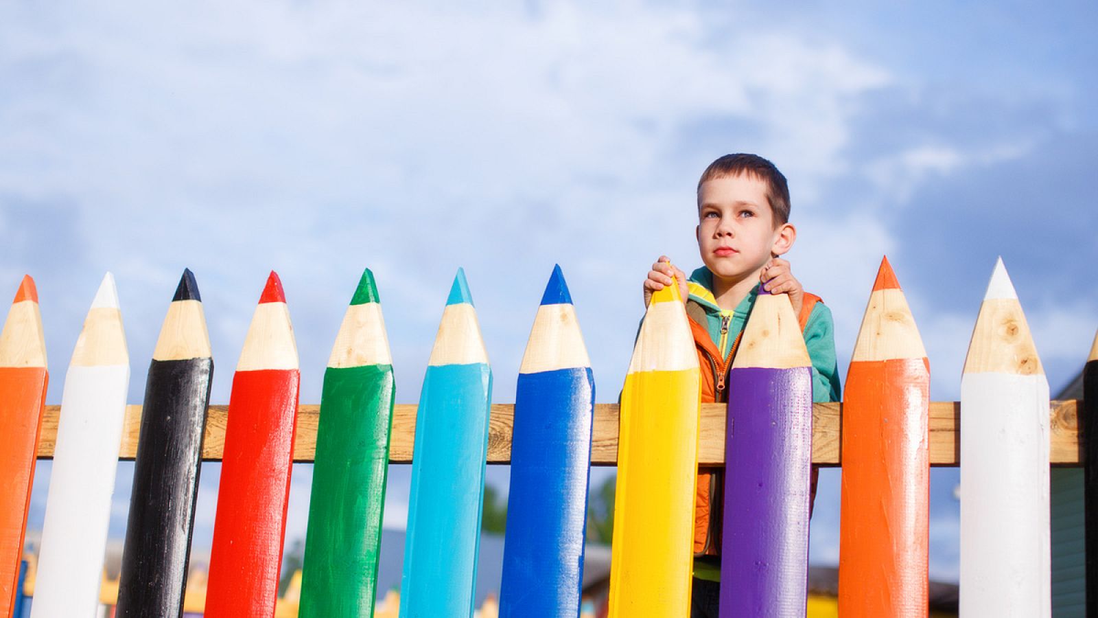Un niño se asoma a la valla de un parque infantil