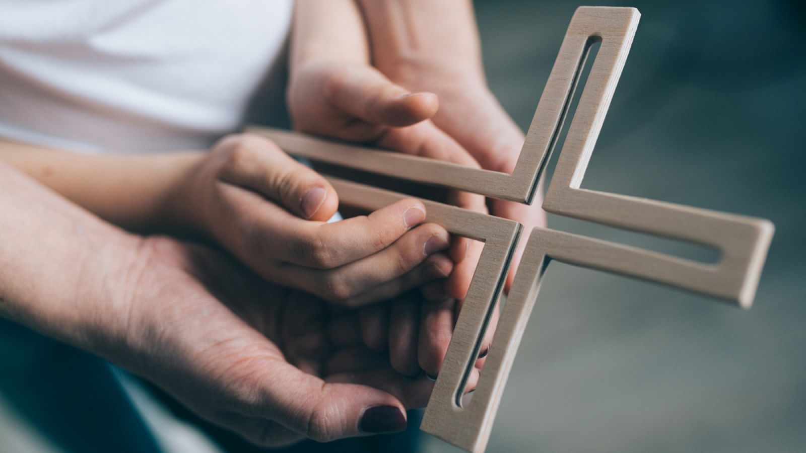 Un adulto reza a una cruz junto a un niño