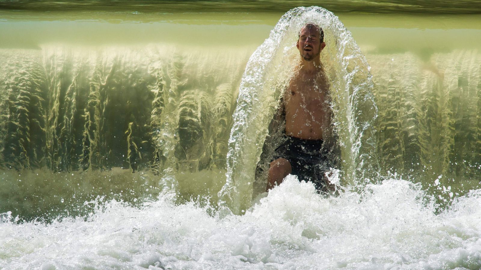 Un hombre se refresca en una pequeña cascada en el arroyo Eisbach, en Múnich