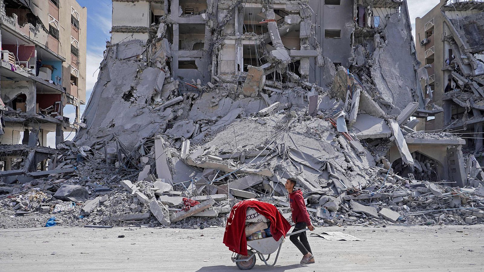 Un palestino empuja una carretilla cargada con sus pertenencias entre los escombros de las casas destruidas por los bombardeos