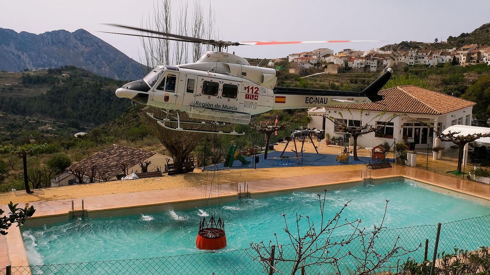 Un helicóptero de los Servicios de Emergencia carga agua en una piscina durante los trabajos de extinción del incendio forestal de Tárbena