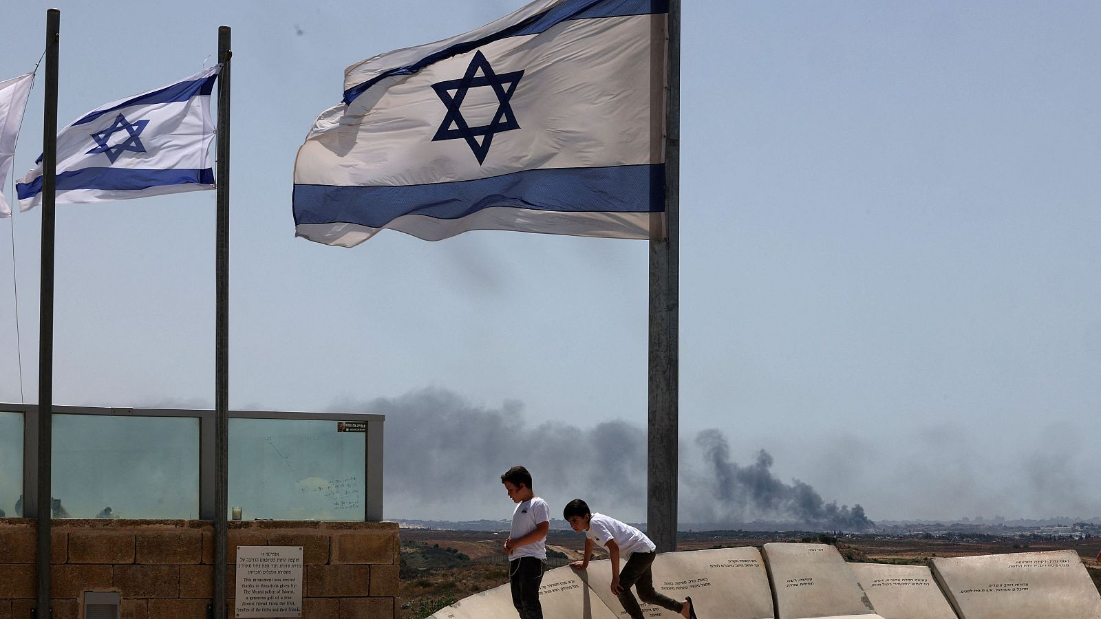 Banderas de Israel y de fondo humo de los bombardeos del ejército israelí sobre Gaza