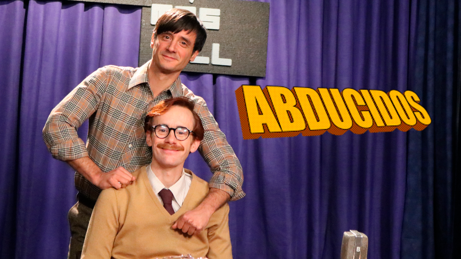 Promoción con dos hombres, uno de pie y otro sentado, ante una cortina morada. El título "ABDUCIDOS" en letras amarillas destaca sobre el fondo.  Estética retro.