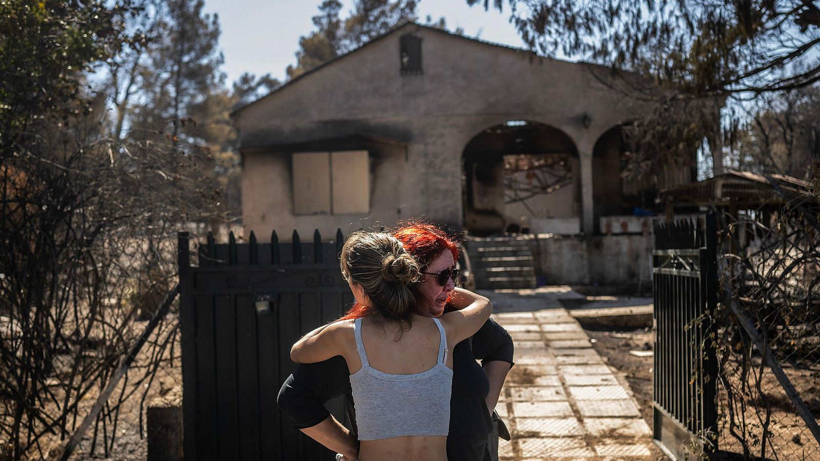 Unos familiares se consuelan mutuamente frente a su casa calcinada por el incendio que ha afectado a los suburbios de Chalandri.
