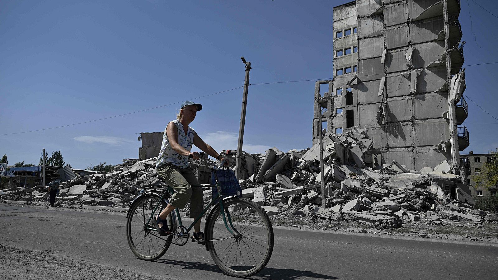 Una mujer pasa en bicicleta junto a los escombros de un edificio de varias plantas en la ciudad de Myrnohrad.