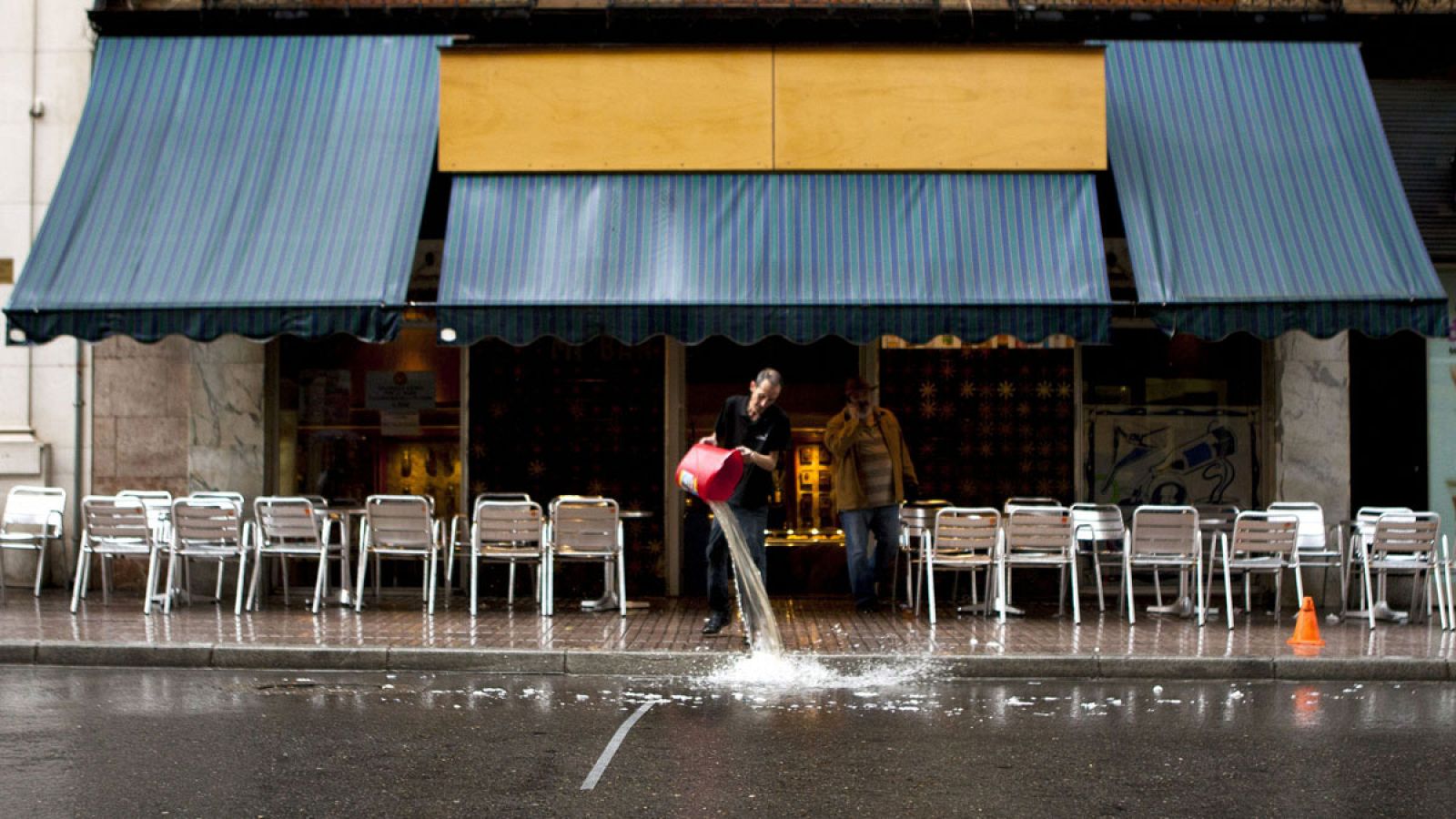 Un empleado de un bar en Huesca vacía un cubo de agua a la puerta del establecimiento