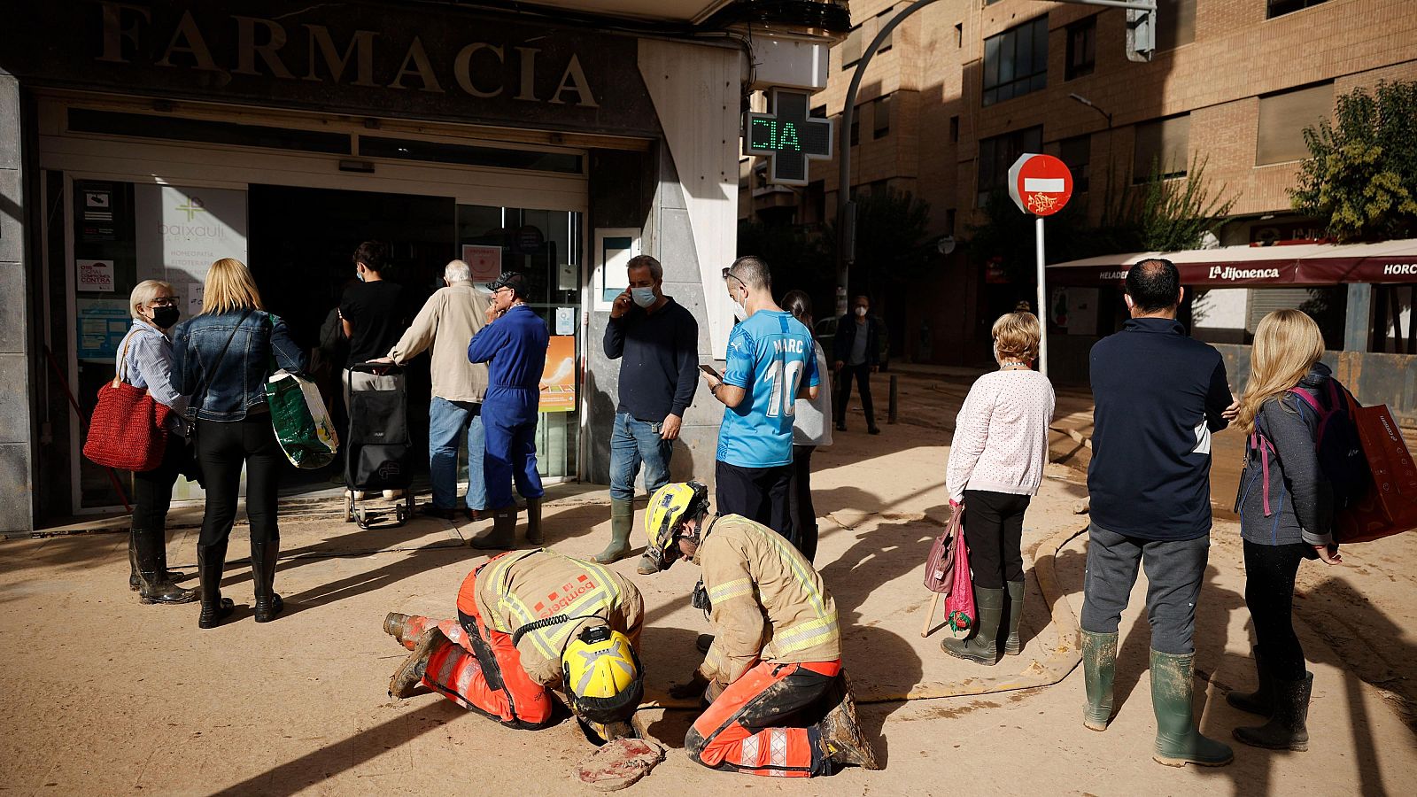 Bomberos trabajan en una calle inundada de Valencia tras el paso de la DANA, mientras vecinos observan.
