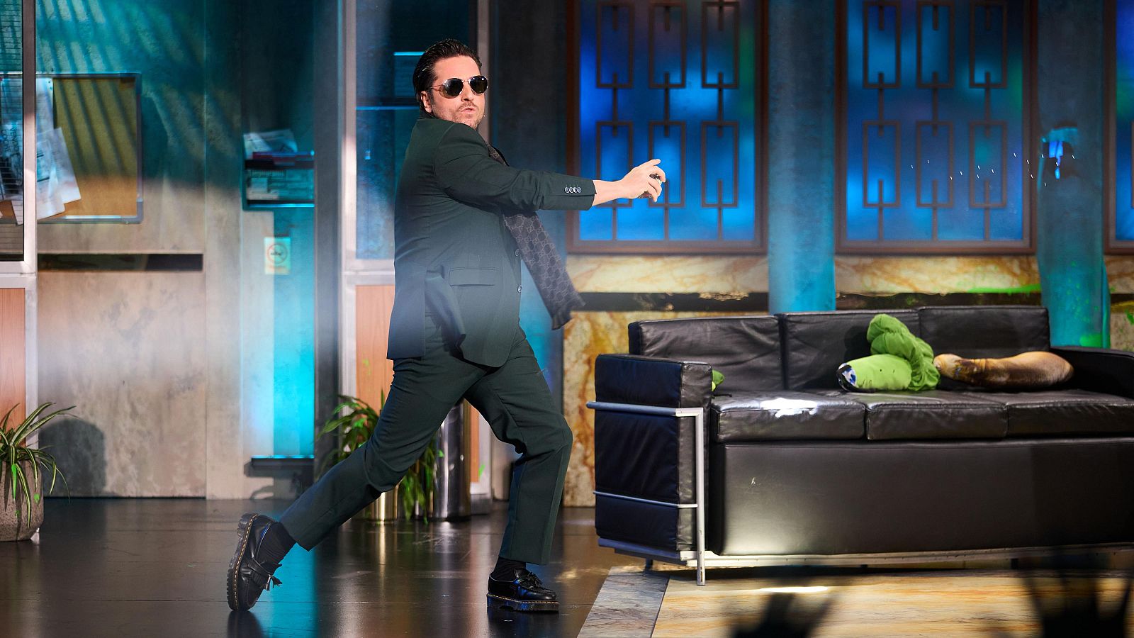 David Bustamante con gafas de sol y traje, en una pose dinámica en el plató de La Resistencia.