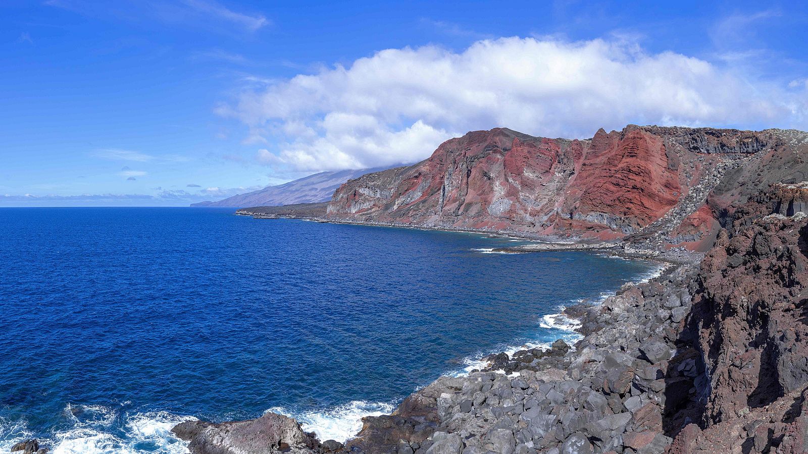 El Mar de las Calmas en El Hierro, con acantilados rocosos, un mar azul y montañas rojizas al fondo
