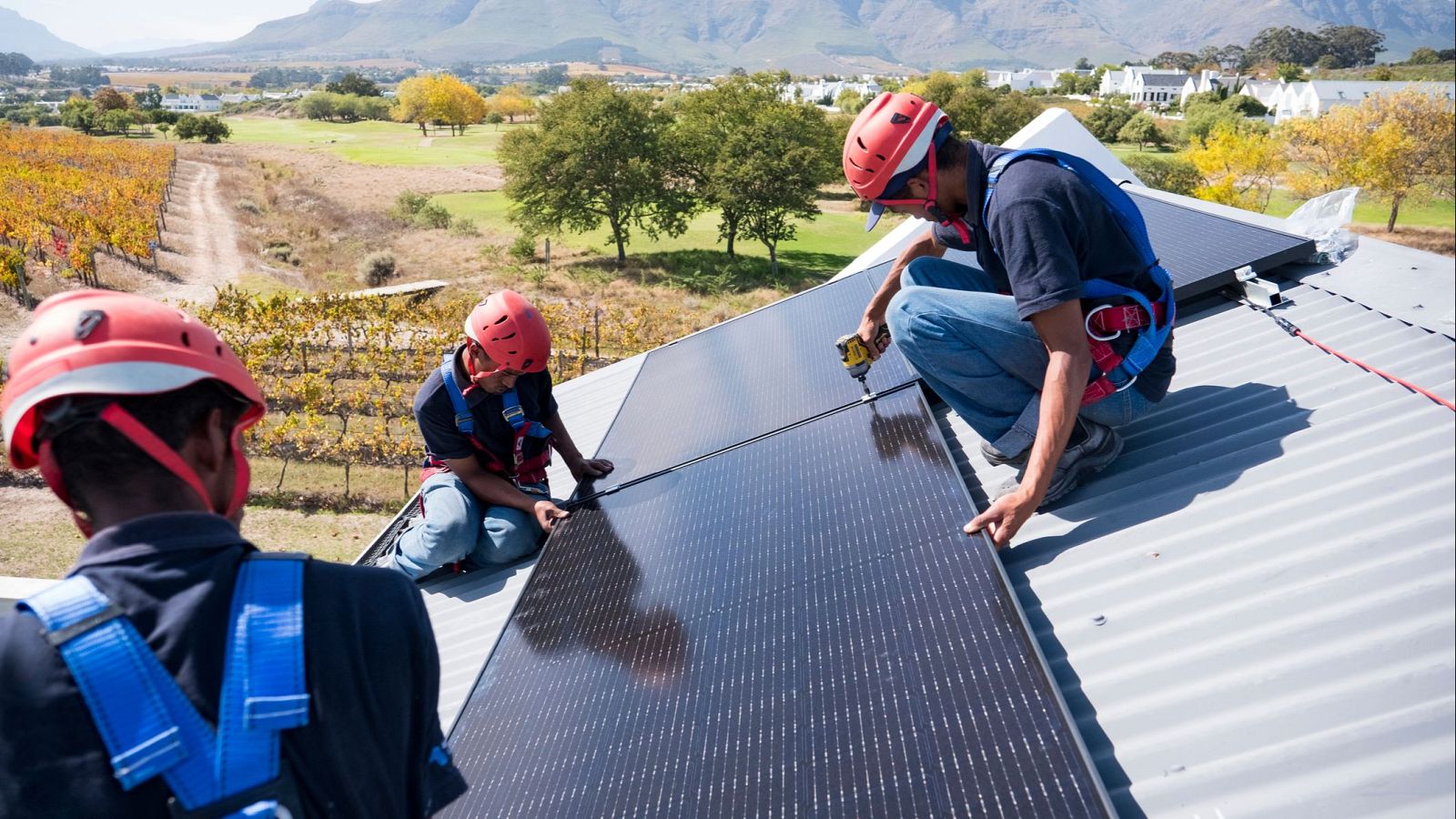 Técnicos con equipo de seguridad instalan paneles solares en un tejado.