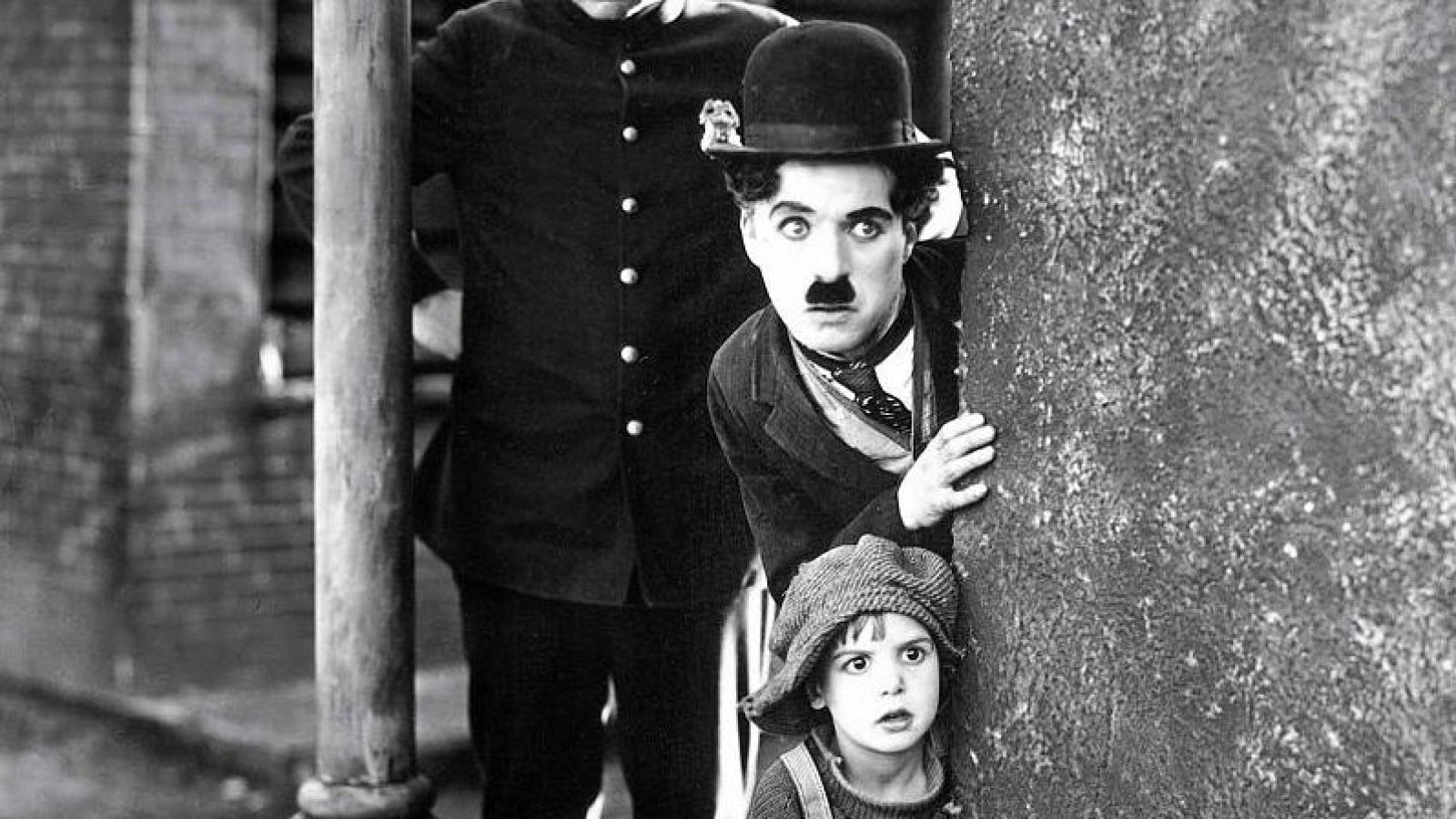 Charlie Chaplin, conocido como Charlot, se esconde tras un muro junto a un niño en una escena de la película 'The Kid'.