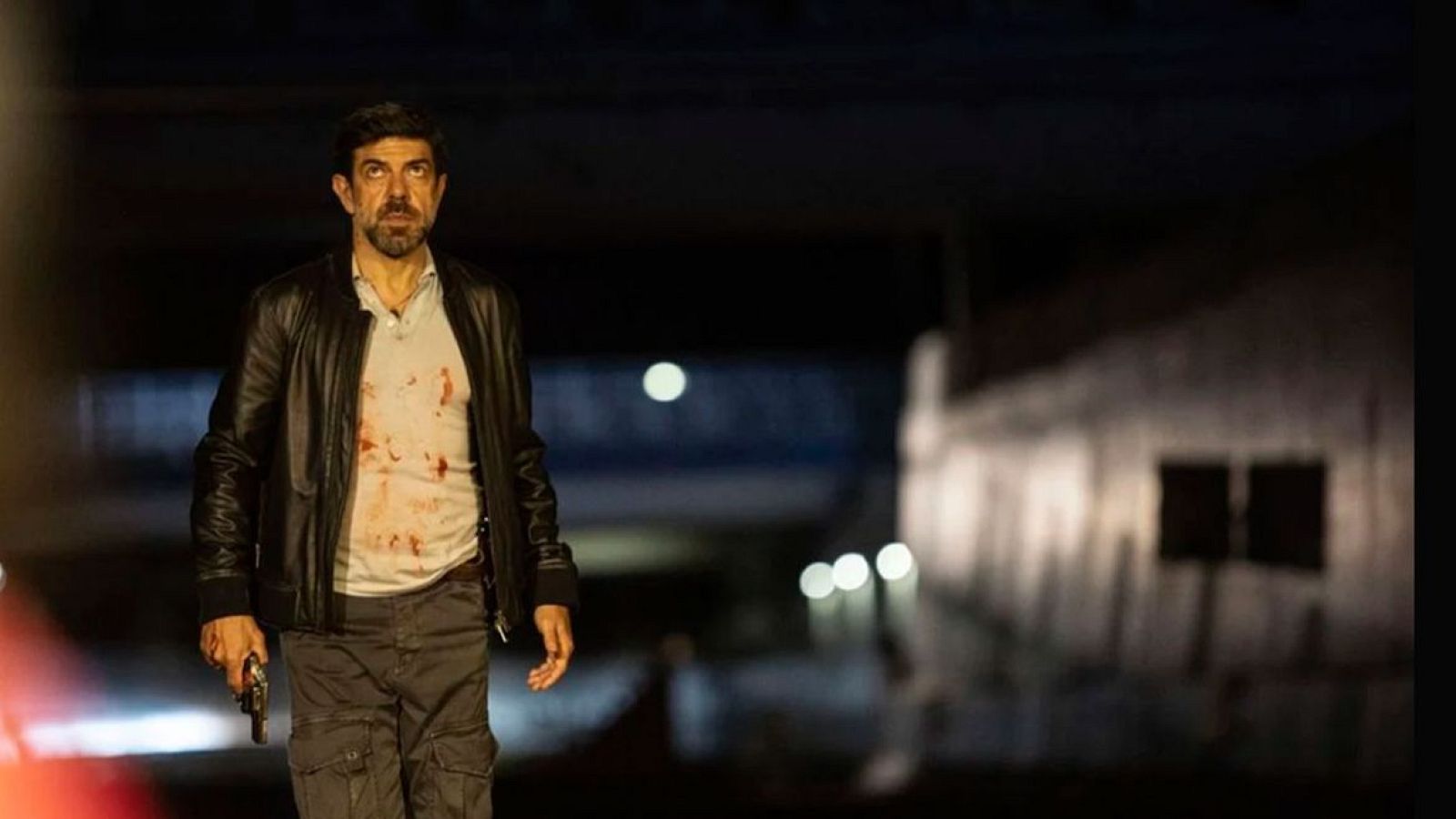 Óscar Jaenada, con la camiseta ensangrentada y una pistola, en una escena nocturna de la película 'Última noche en Milán'.