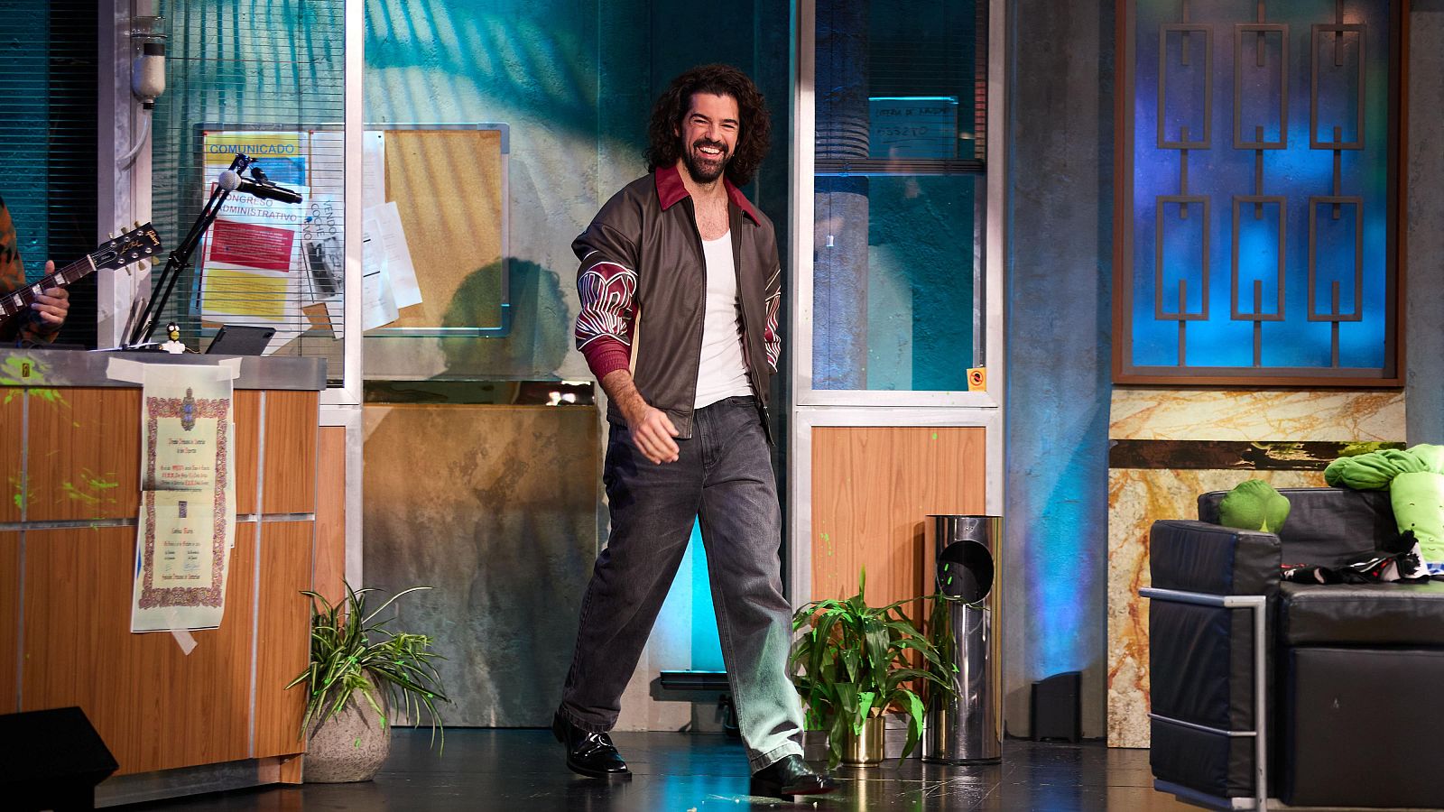 Imagen de Miguel Ángel Muñoz en el programa "La Revuelta". El actor sonríe mientras camina por el decorado del programa, que parece una oficina con elementos retrofuturistas.
