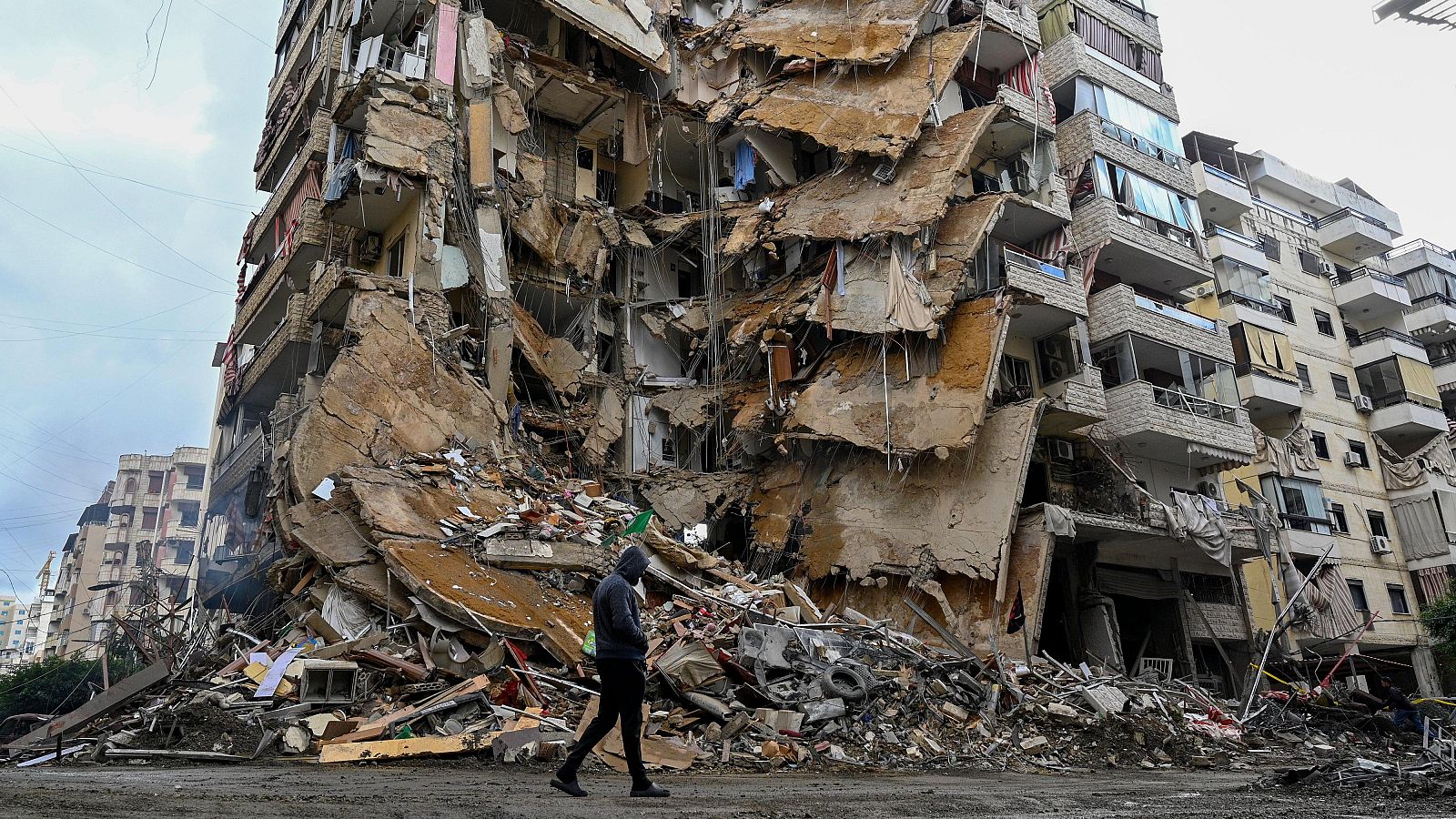 Edificio residencial dañado en Tayouneh, Beirut, tras un ataque aéreo. Escombros y un hombre caminando frente a la destrucción.