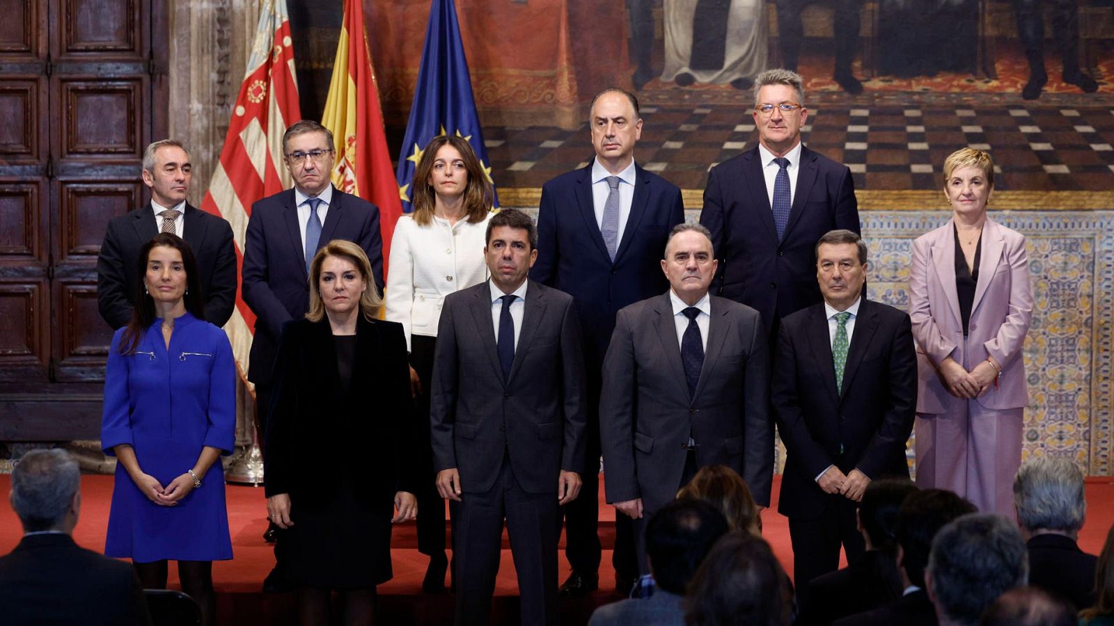 Carlos Mazón preside la toma de posesión de cuatro nuevos consejeros del Consell Valenciano.  Grupo formalmente vestido con banderas de España, Comunidad Valenciana y UE al fondo.