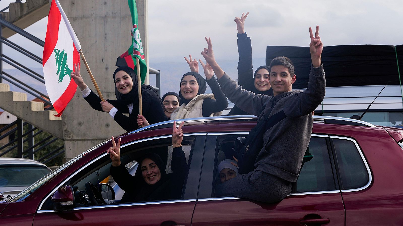 Familias libanesas celebran el alto el fuego desde un coche, ondeando banderas y haciendo gestos de paz.  El equipaje en el techo indica su regreso a casa.