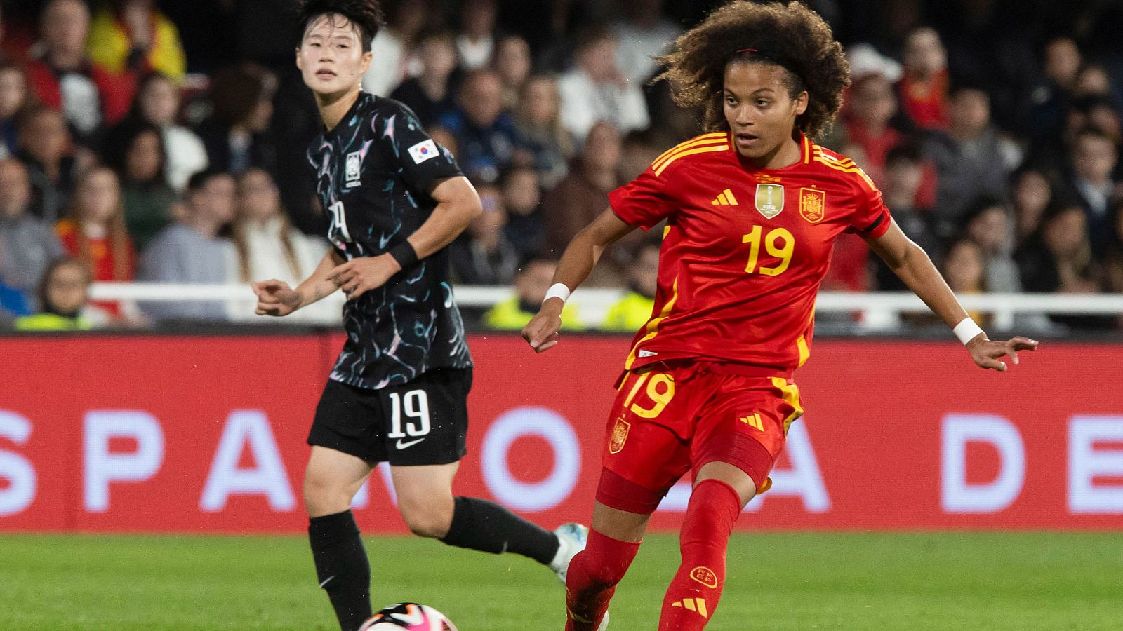 Vicky López (España #19) controla el balón en un partido contra Corea del Sur. Una jugadora coreana intenta defenderla.