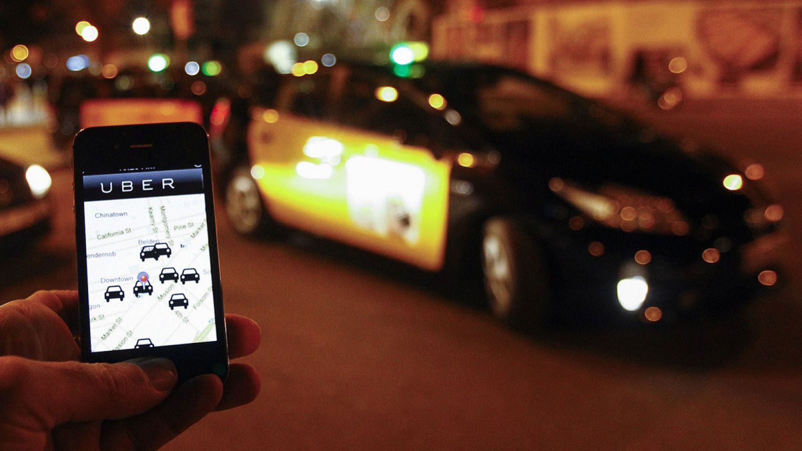 La aplicación para móviles de Uber en un smartphone junto a una cola de personas que esperan para coger un taxi