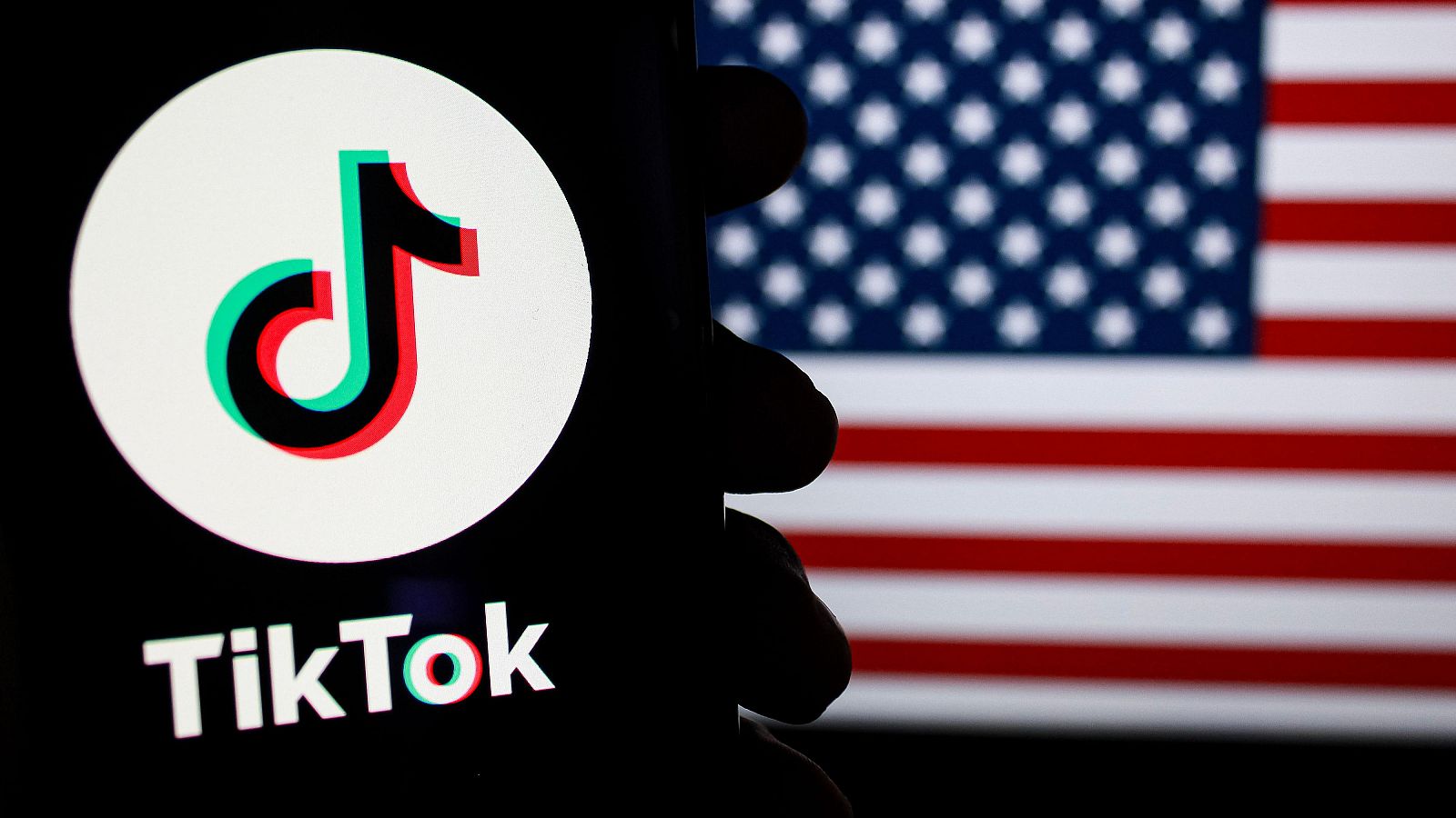 El logo de la red social TikTok en la pantalla de un móvil y con la bandera estadounidense de fondo