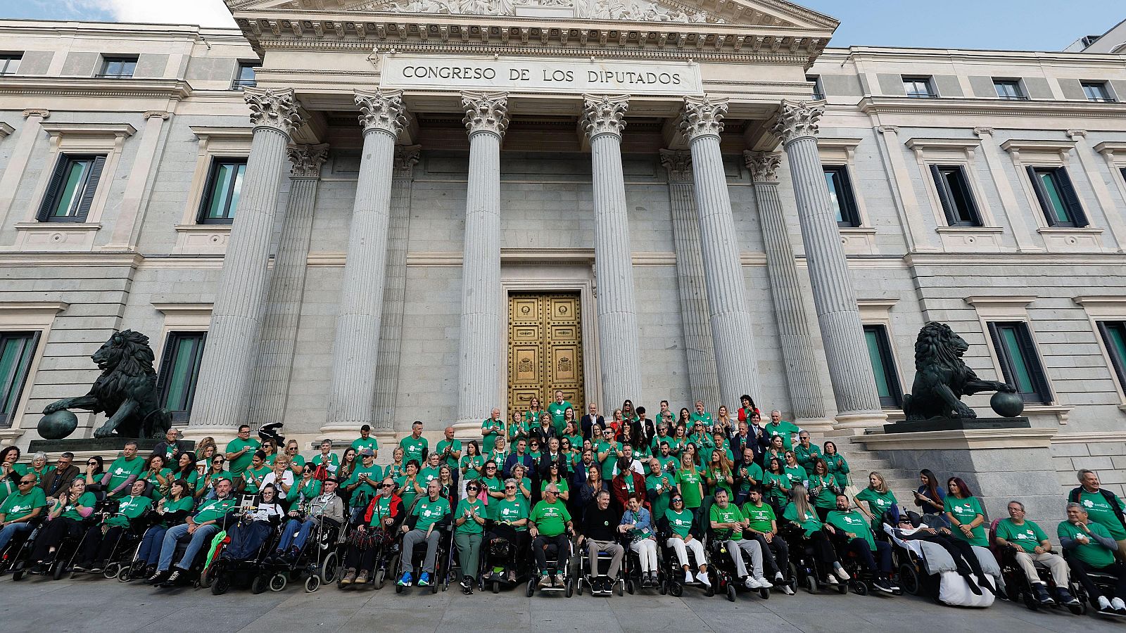 Manifestación frente al Congreso de los Diputados. Personas en sillas de ruedas con camisetas verdes celebran un logro legislativo.