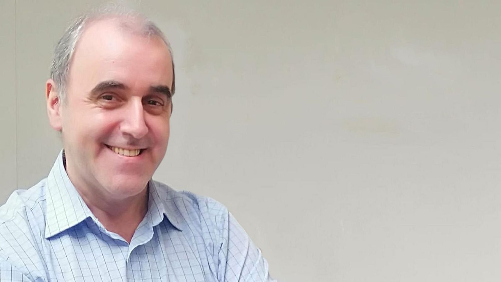 Retrato de un hombre de mediana edad, con pelo canoso y camisa a cuadros, sonriendo a cámara.