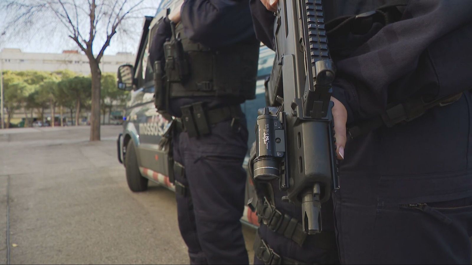 Agentes antidisturbios con uniformes negros, chalecos y armas largas patrullan una zona con presencia policial.