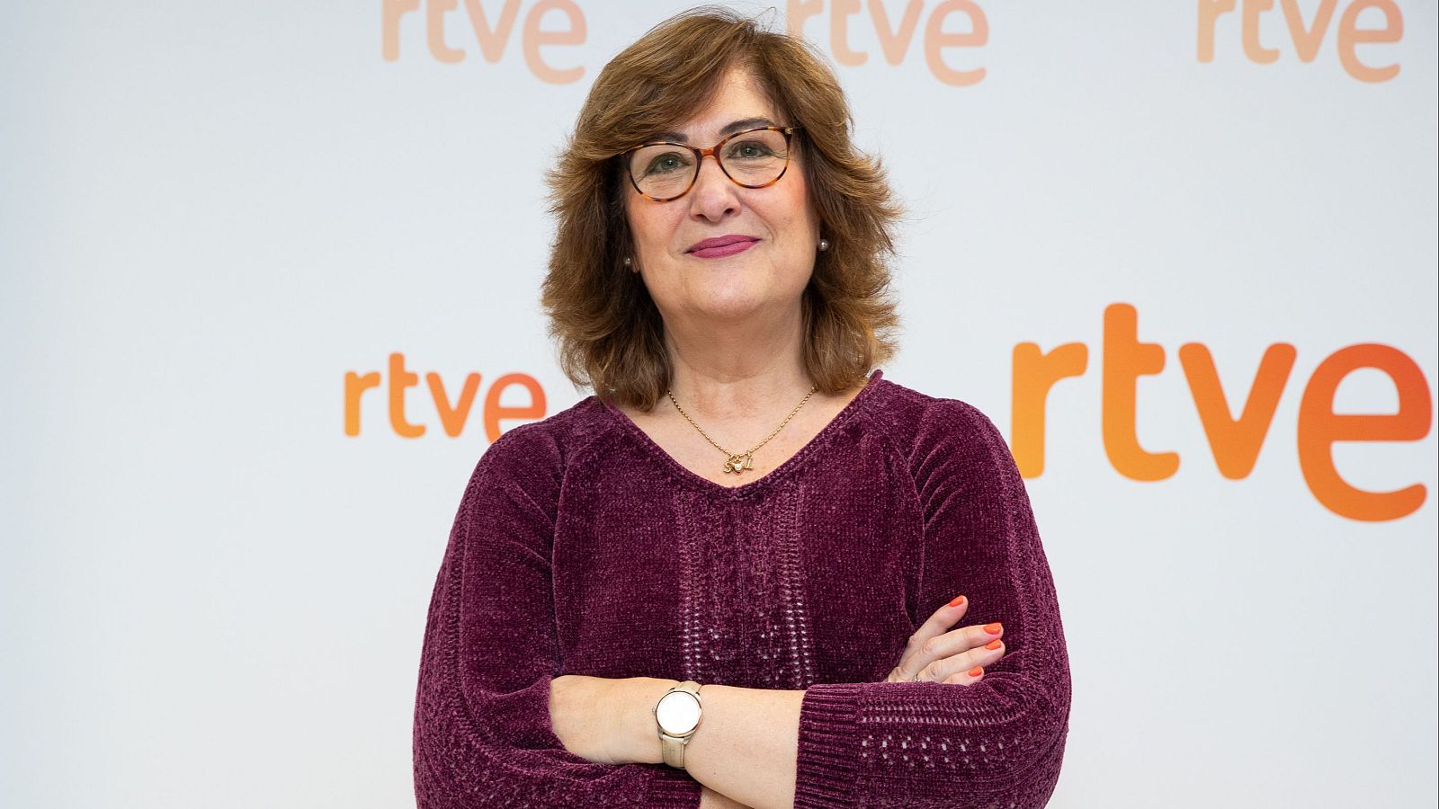 Ana Cerrada, de Comunicación RTVE, en foto corporativa: jersey granate, gafas, brazos cruzados, fondo con logo RTVE.
