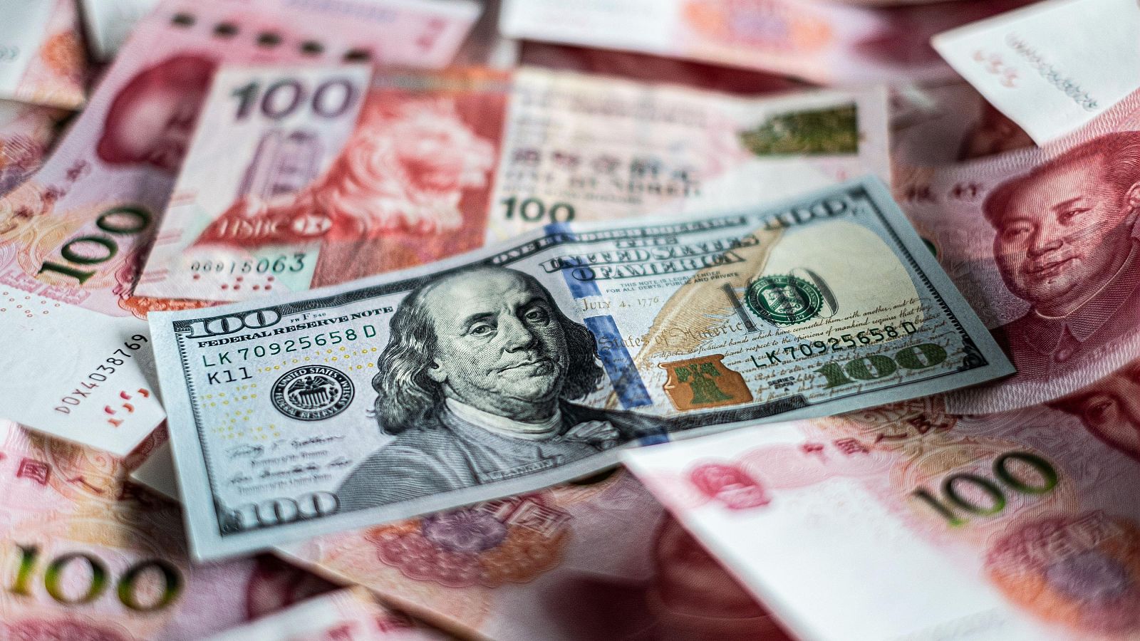 Billete de 100 dólares sobre billetes de 100 yuanes chinos;  los retratos de Benjamin Franklin y Mao Zedong ilustran la relación económica entre ambos países, sugiriendo tensiones comerciales.