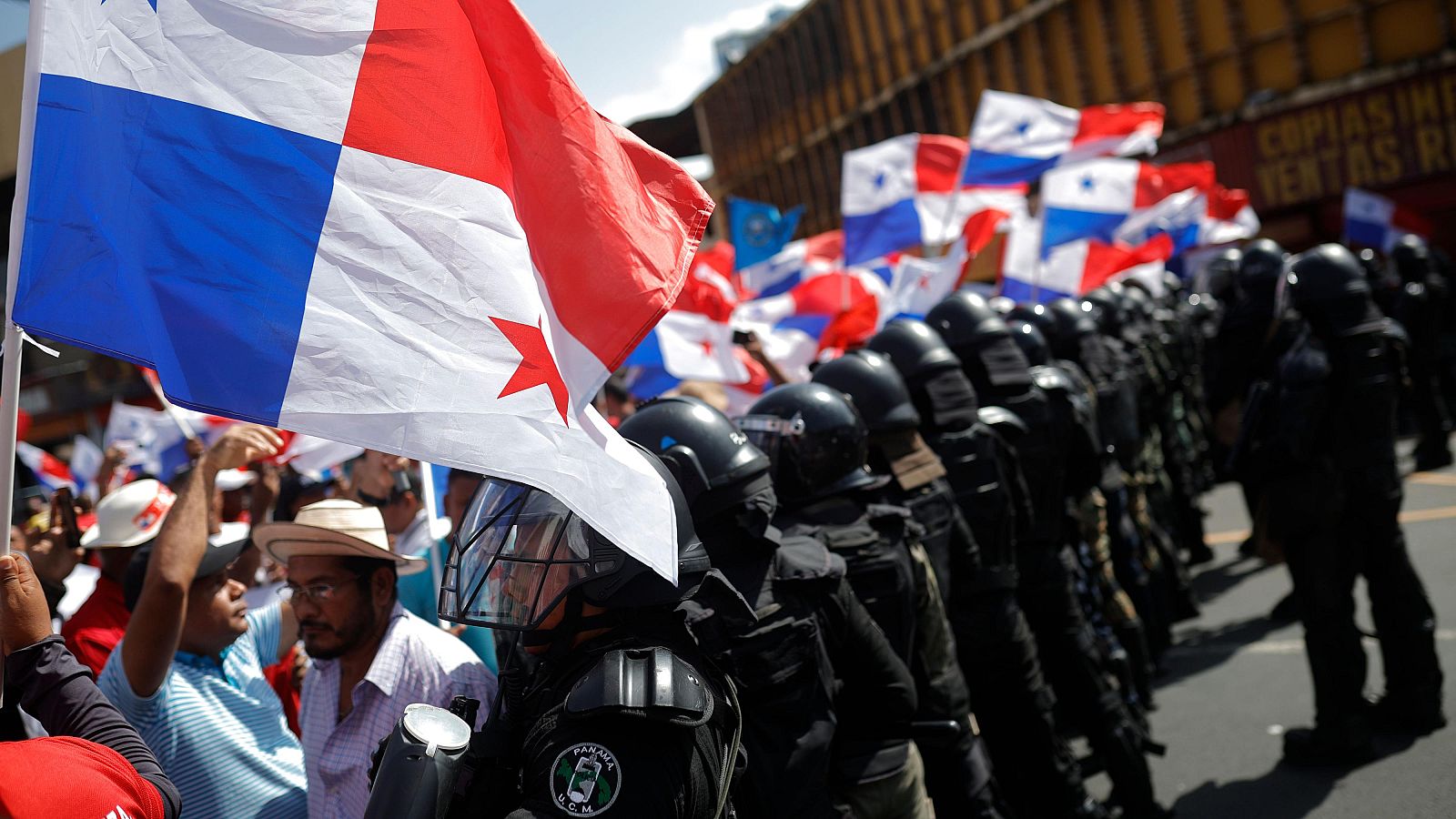 Un grupo de personas protesta frente a unidades antidisturbios por la visita del Secretario de Estado de Estados Unidos, Marco Rubio