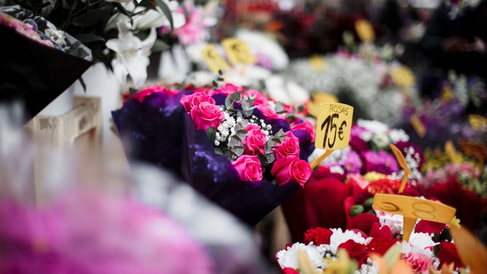 Ramos de flores, principalmente rosas rosas con cartel de precio (15€), junto a lirios blancos y otras flores de colores vibrantes.