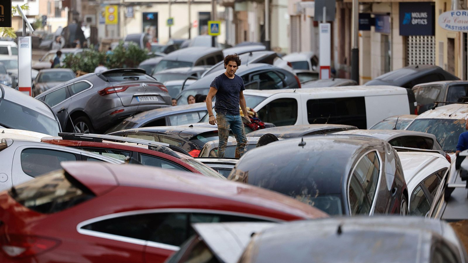 Graves inundaciones en Valencia dejan coches apilados y cubiertos de lodo. Un hombre inspecciona los daños caminando sobre los vehículos.