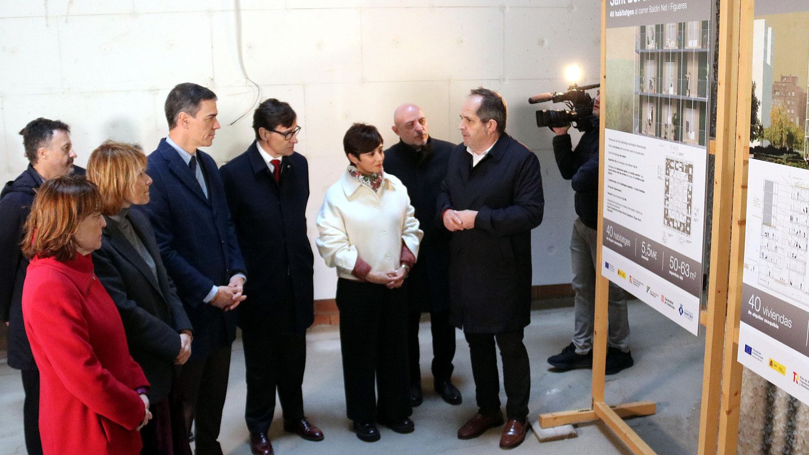 Visita de autoridades a obra de viviendas públicas.  El presidente escucha explicaciones del arquitecto, quien señala planos mostrando detalles del proyecto (40 viviendas, 50-63m², 5,5M€).