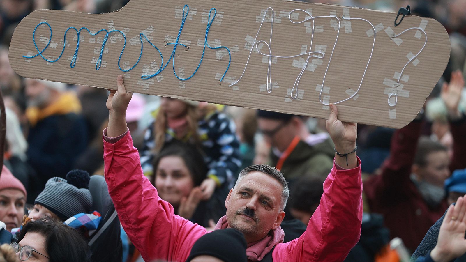 Manifestante con bigote estilo Hitler protesta contra el partido AfD en Alemania, mostrando un cartel con la pregunta irónica: "¿En serio? AfD"