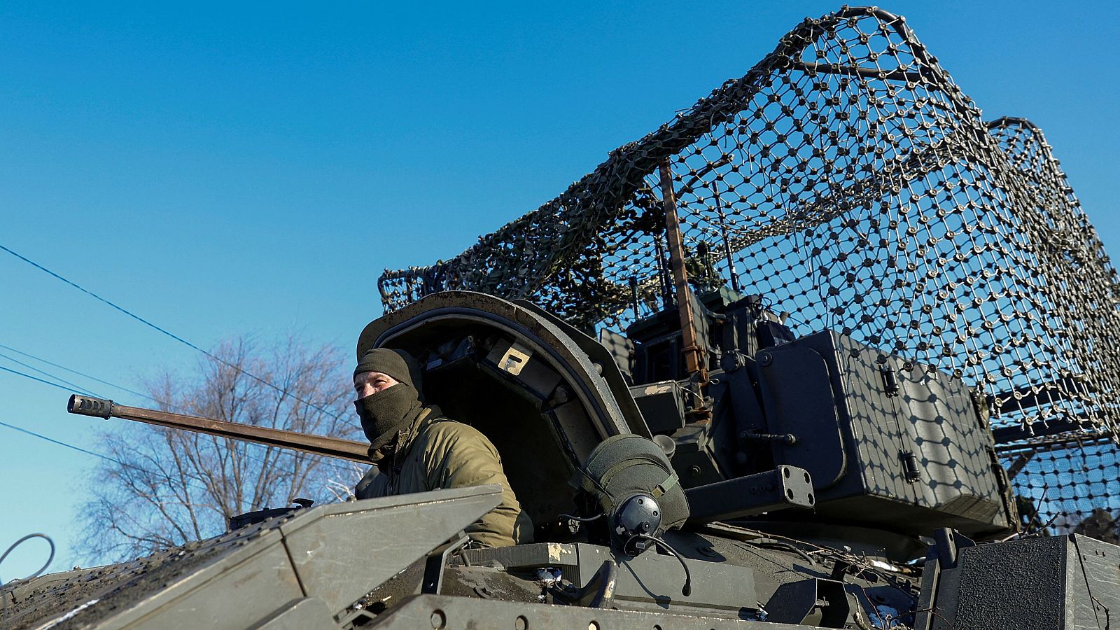 Soldado en vehículo militar camuflado, alerta y mirando a la izquierda.  Invierno, posible zona de conflicto cerca de una aldea.