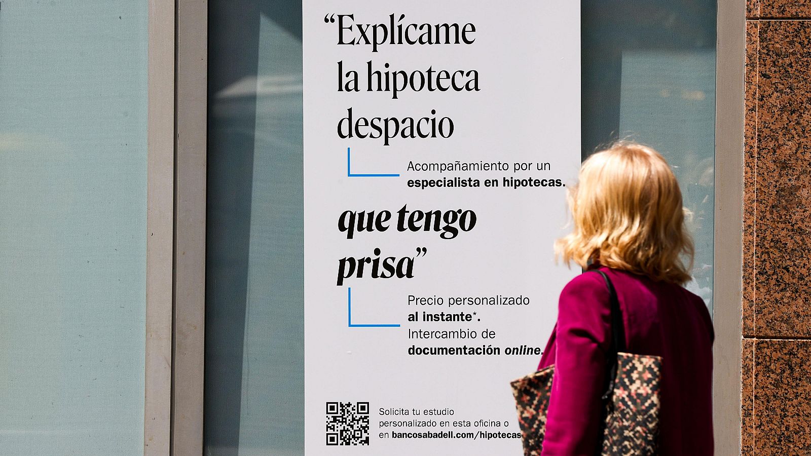 Una mujer ante un cartel bancario sobre las hipotecas.