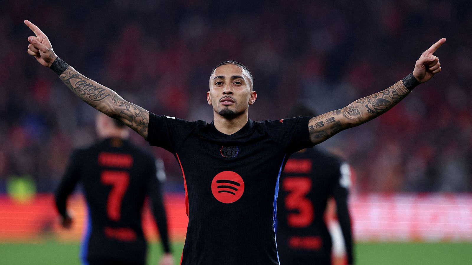 Celebración de Héctor Bellerín con la camiseta del Barça (logo Spotify visible), brazos extendidos y dedos índices arriba.  Numerosos tatuajes en sus brazos.