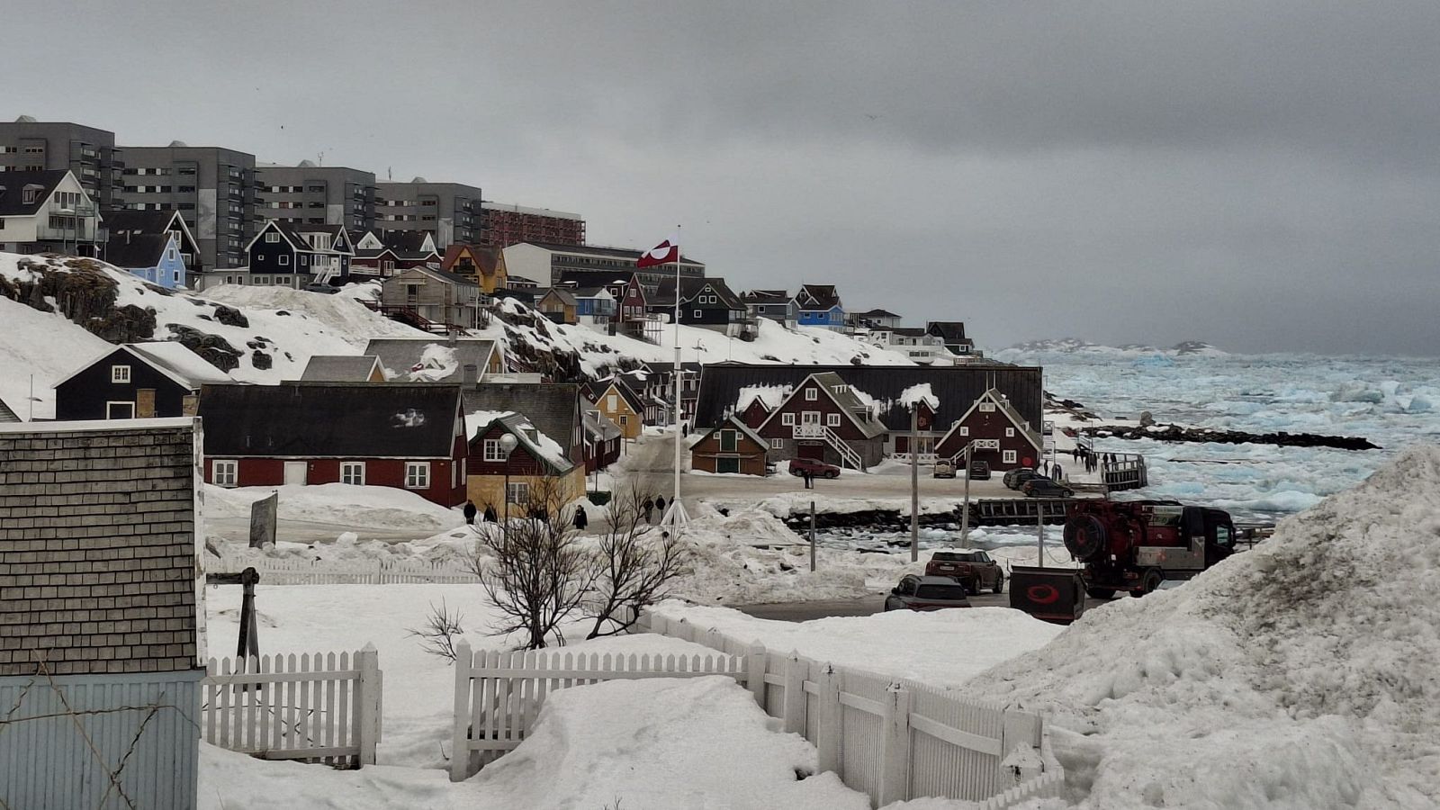 Invierno en Nuuk: casas de colores bajo un cielo gris, nieve en las calles y el mar parcialmente congelado al fondo.