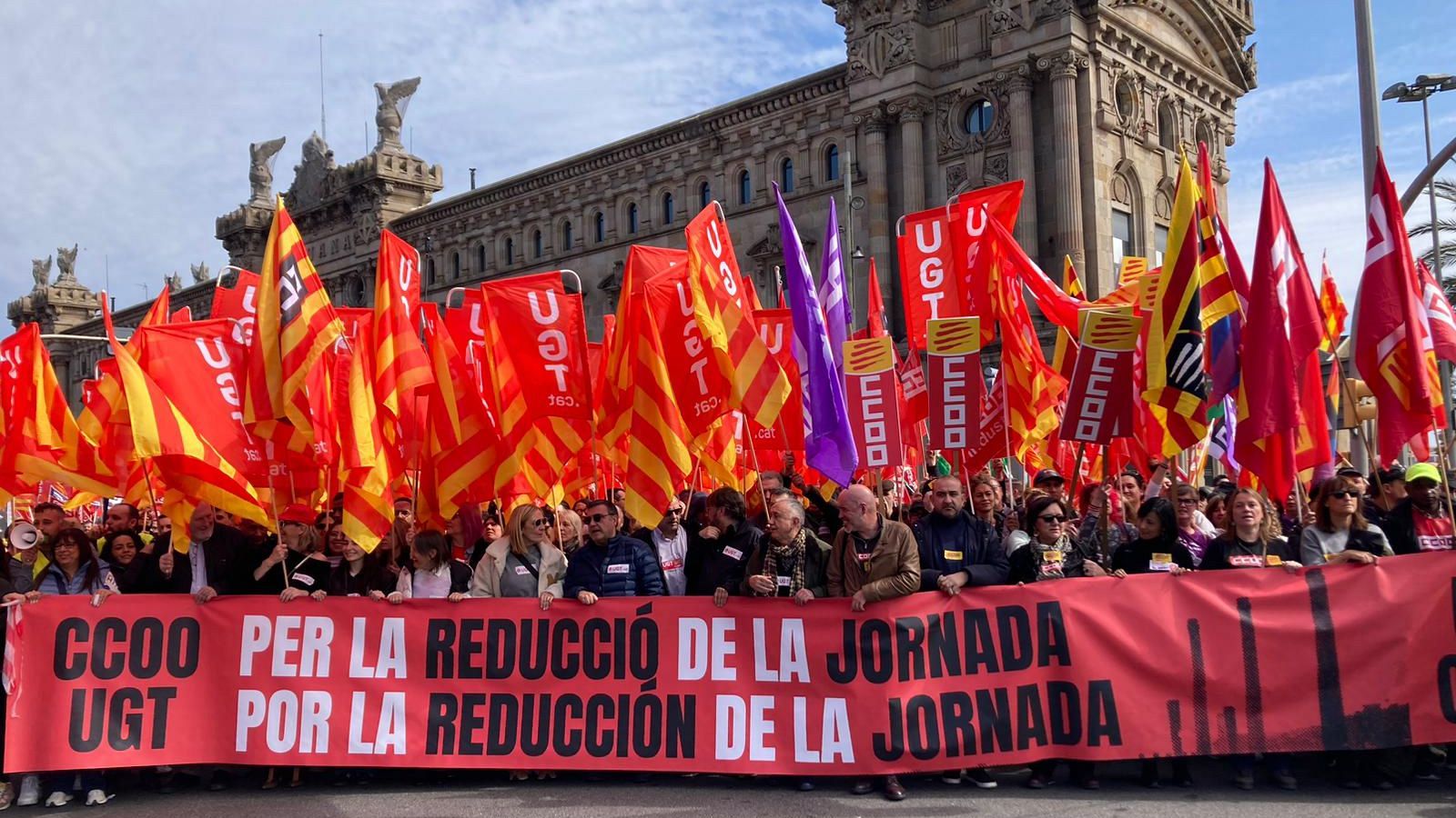 Multitud manifestándose en Barcelona por la reducción de la jornada laboral.  Pancartas de CCOO y UGT reclaman jornadas más cortas.  Numerosas banderas sindicales presentes.