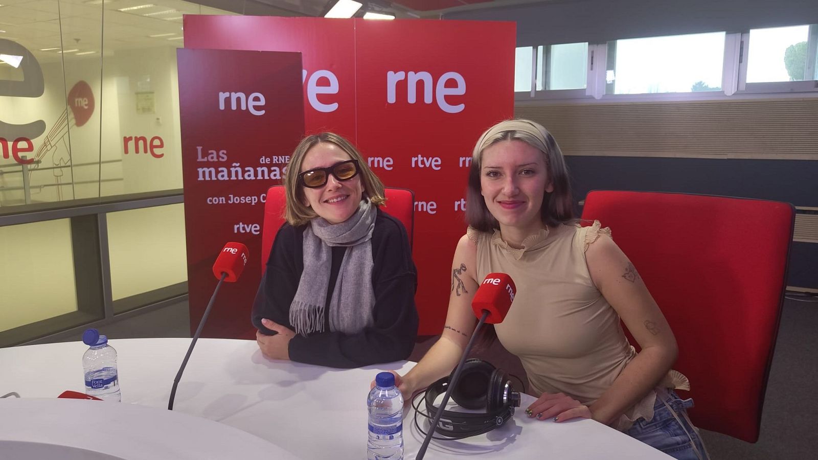 Entrevista en estudio de radio RNE: dos mujeres sentadas ante micrófonos, una botella de agua en la mesa y un panel con el logo de la emisora al fondo.