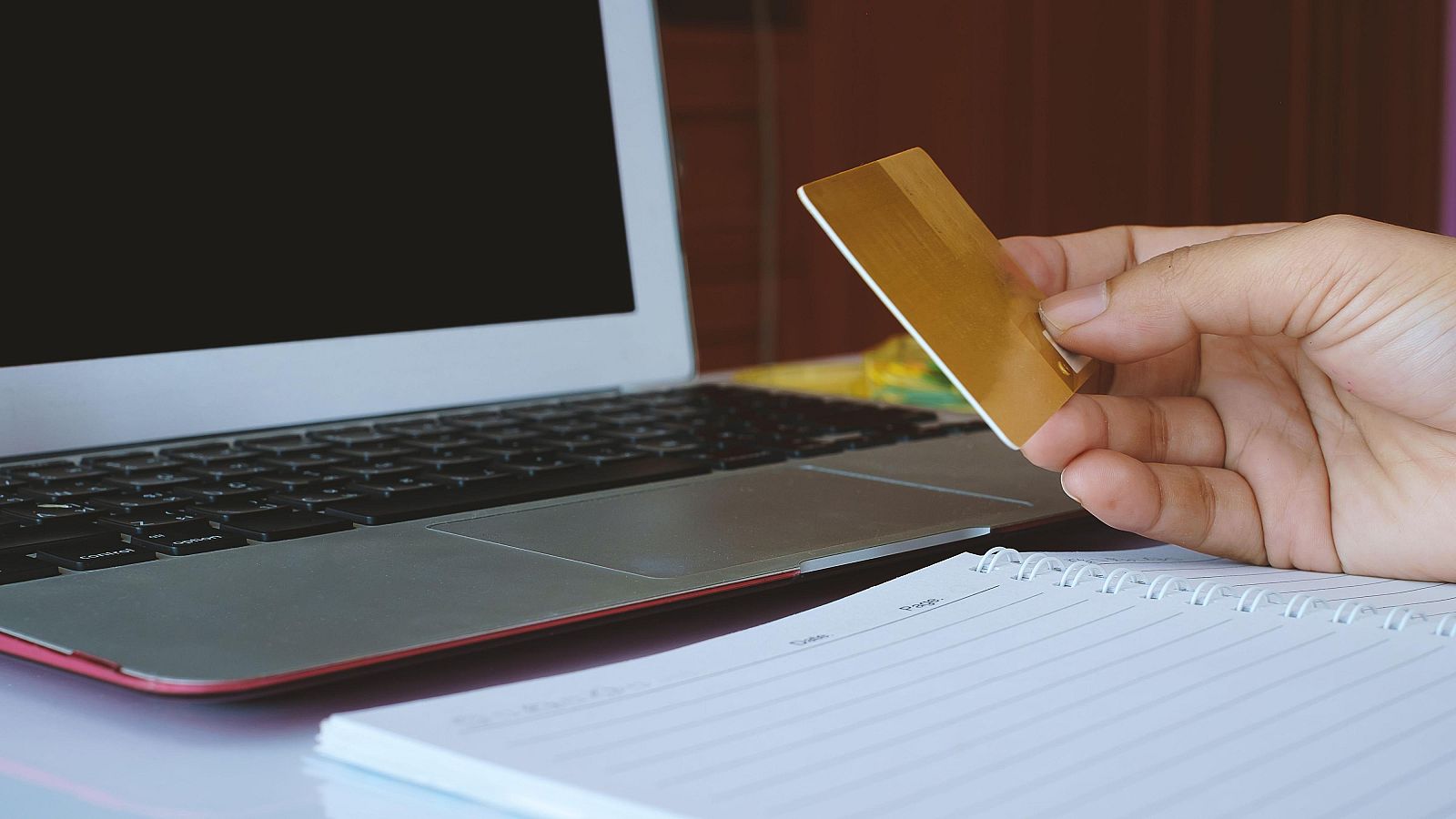 Un hombre sostiene una tarjeta de crédito frente a un ordenador.