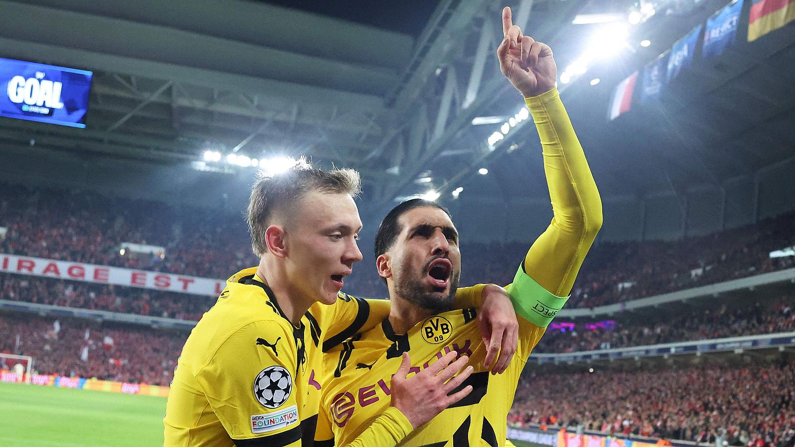 Celebración de gol del Borussia Dortmund en un estadio lleno. Dos jugadores, uno con el brazo en alto, festejan con la afición rival de fondo.