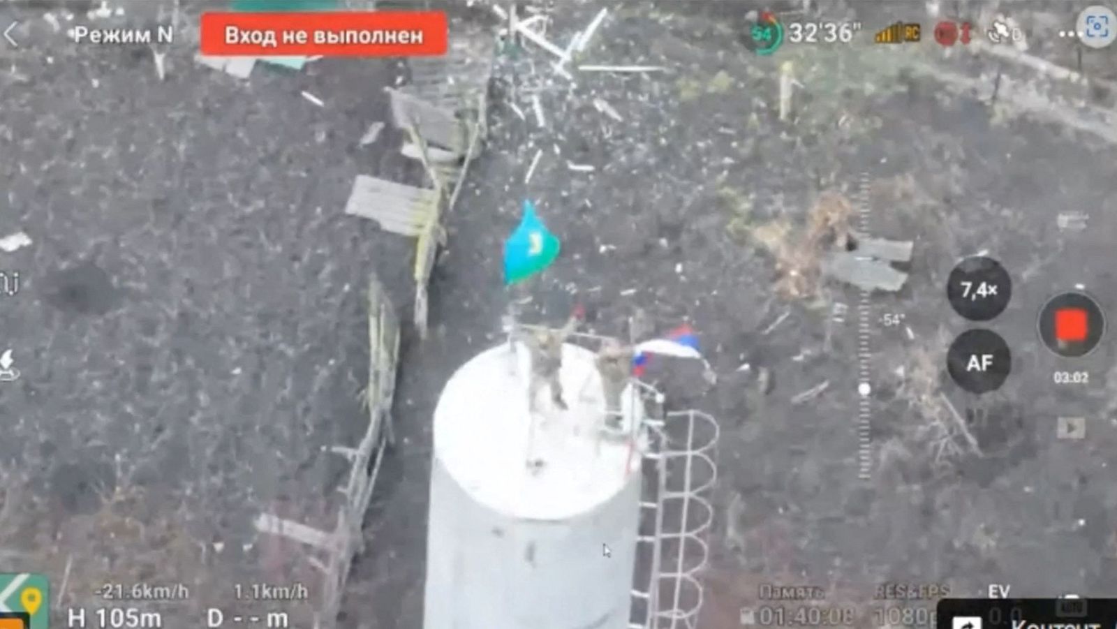 Dos soldados ondeando la bandera rusa en lo alto de una torre de agua en el centro Sudzha, Kursk