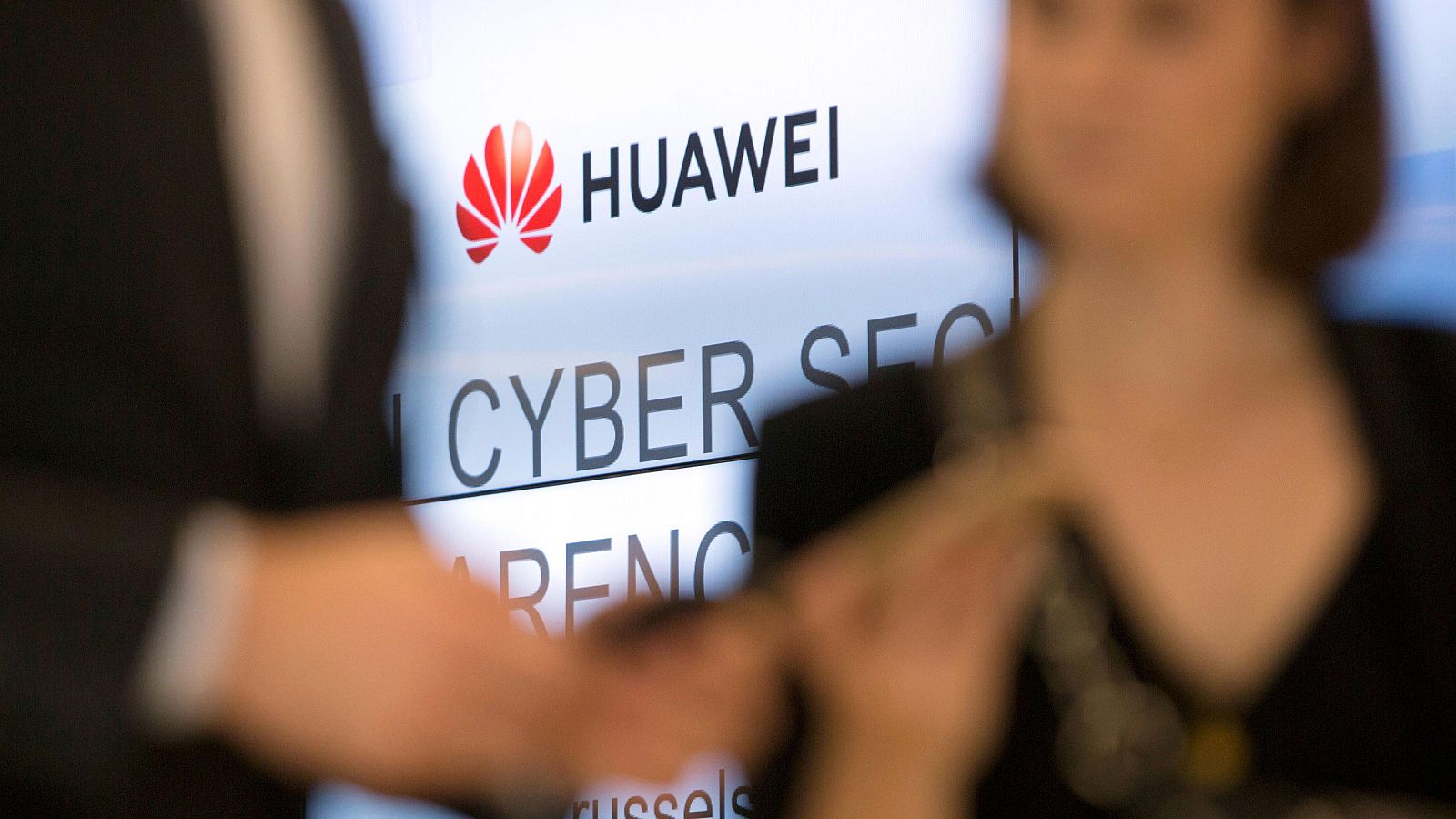 Dos personas miran sus teléfonos delante del logo de Huawei en Bruselas