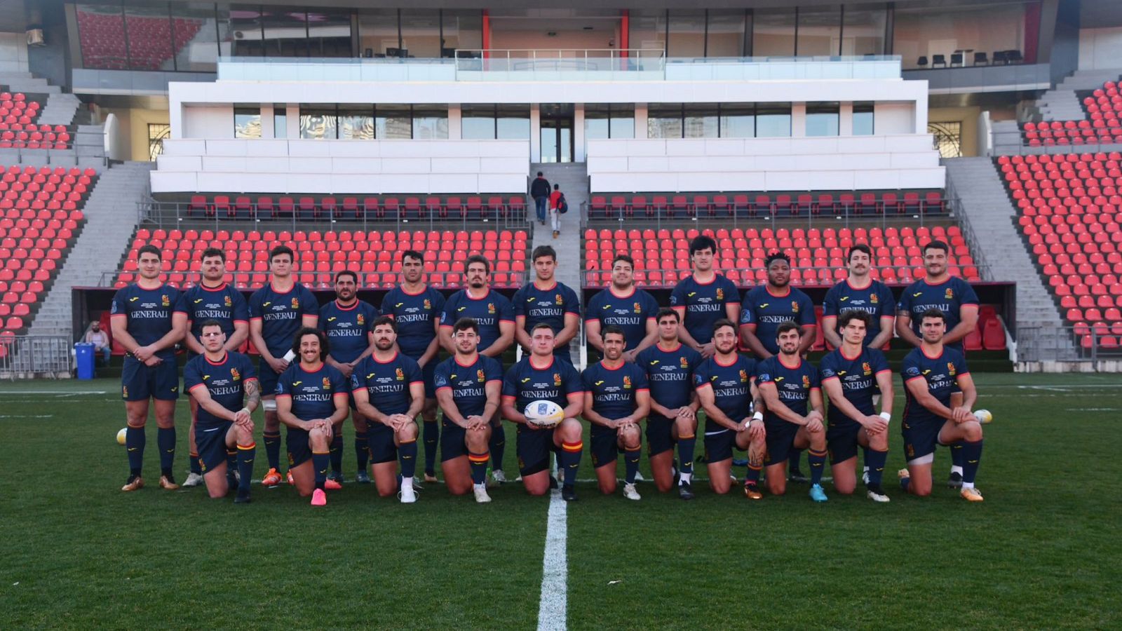 Equipo de rugby español en uniforme azul con detalles amarillo y rojo, posando con un balón.  El patrocinador Generali se ve en sus camisetas.