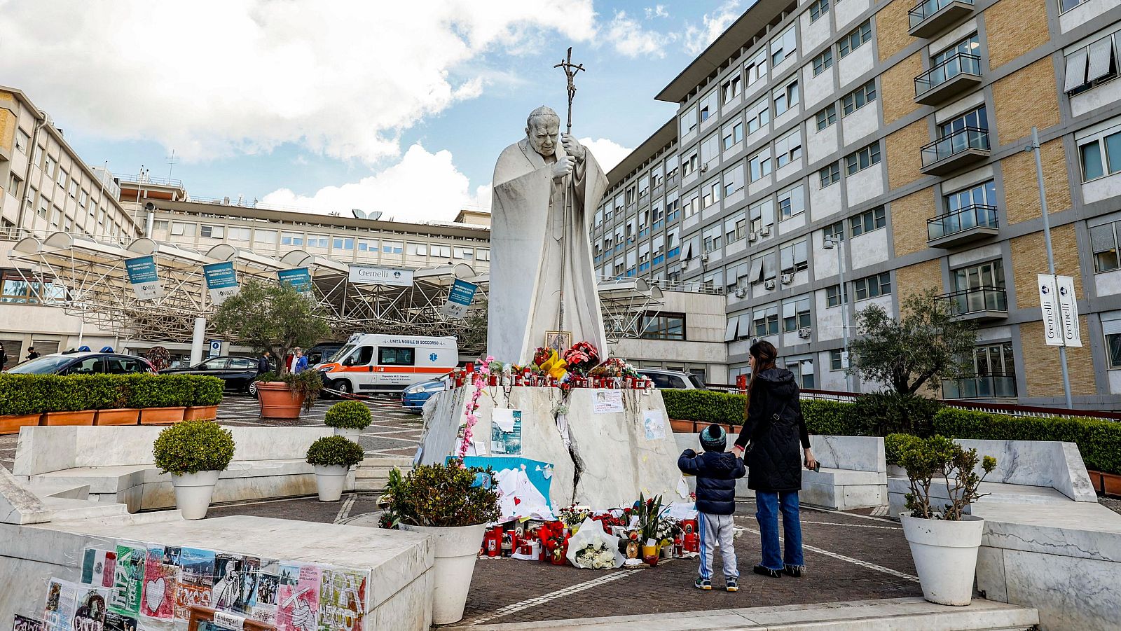 Una mujer y un niño presentan sus respetos frente a la estatua del Papa San Juan Pablo II afuera del Hospital Universitario Gemelli en Roma