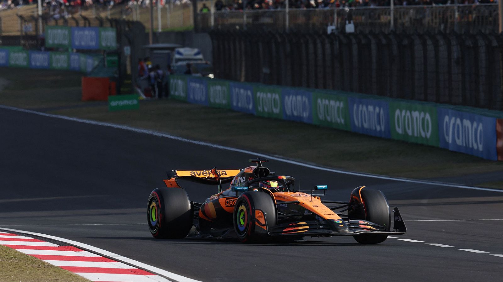 Coche de F1 naranja y negro #81 con patrocinador 'aVerMedia', tomando una curva en una pista con gradas y publicidad al fondo.