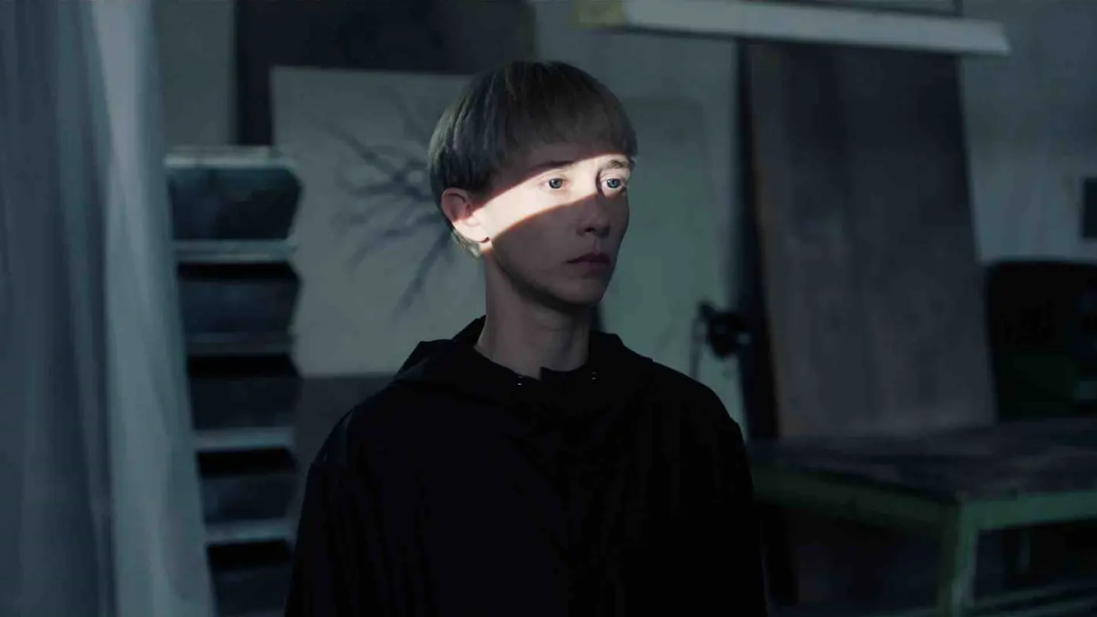 Imagen de Ingrid García-Jonsson, con sudadera negra y cabello rubio, interpretando un papel criminal en una película. Iluminación dramática en su rostro.