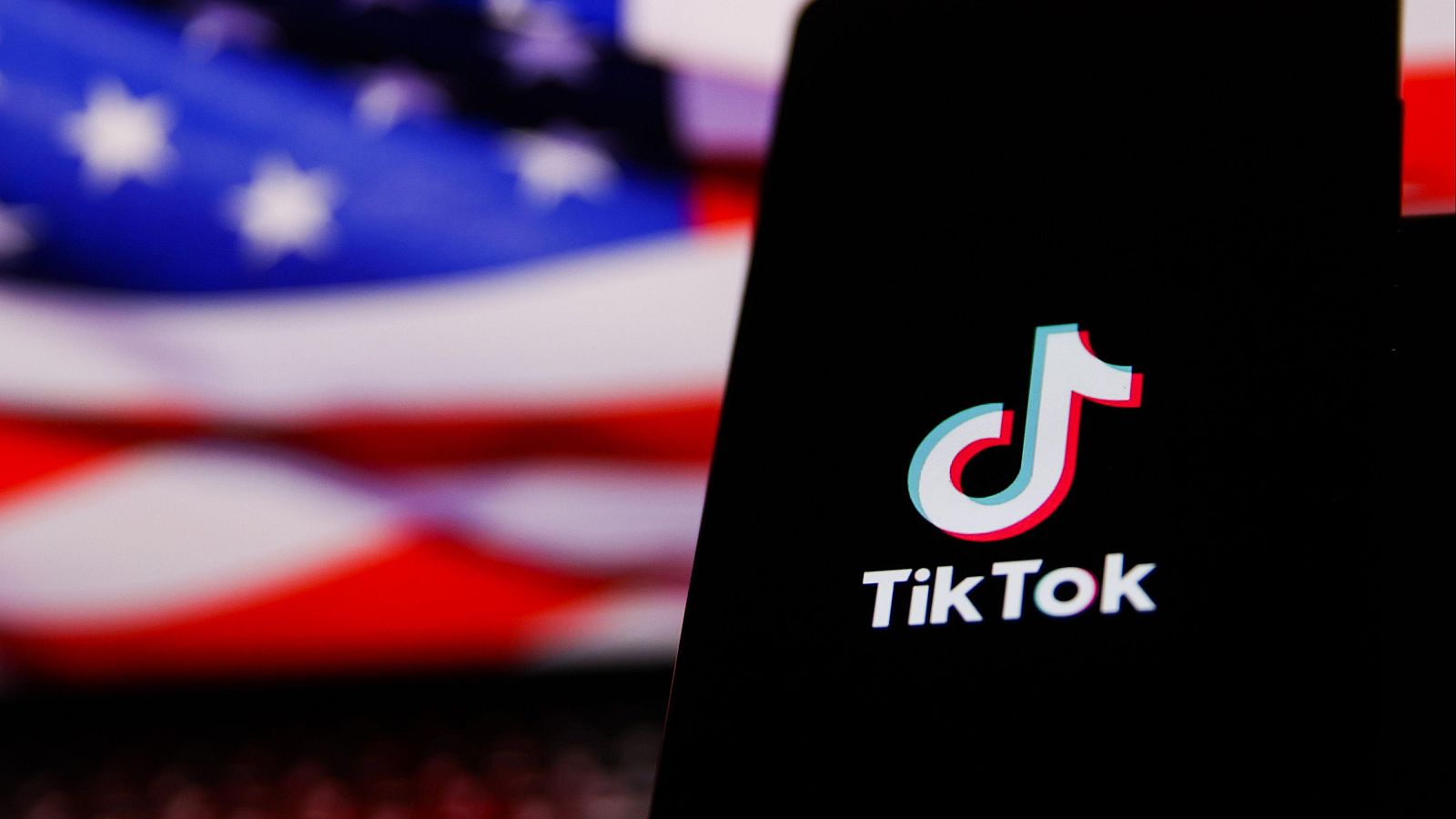 El logo de la red social TikTok en la pantalla de un móvil y con la bandera estadounidense de fondo
